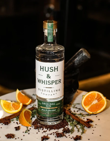 Hush and whisper gin on table next to orange and cinnamon